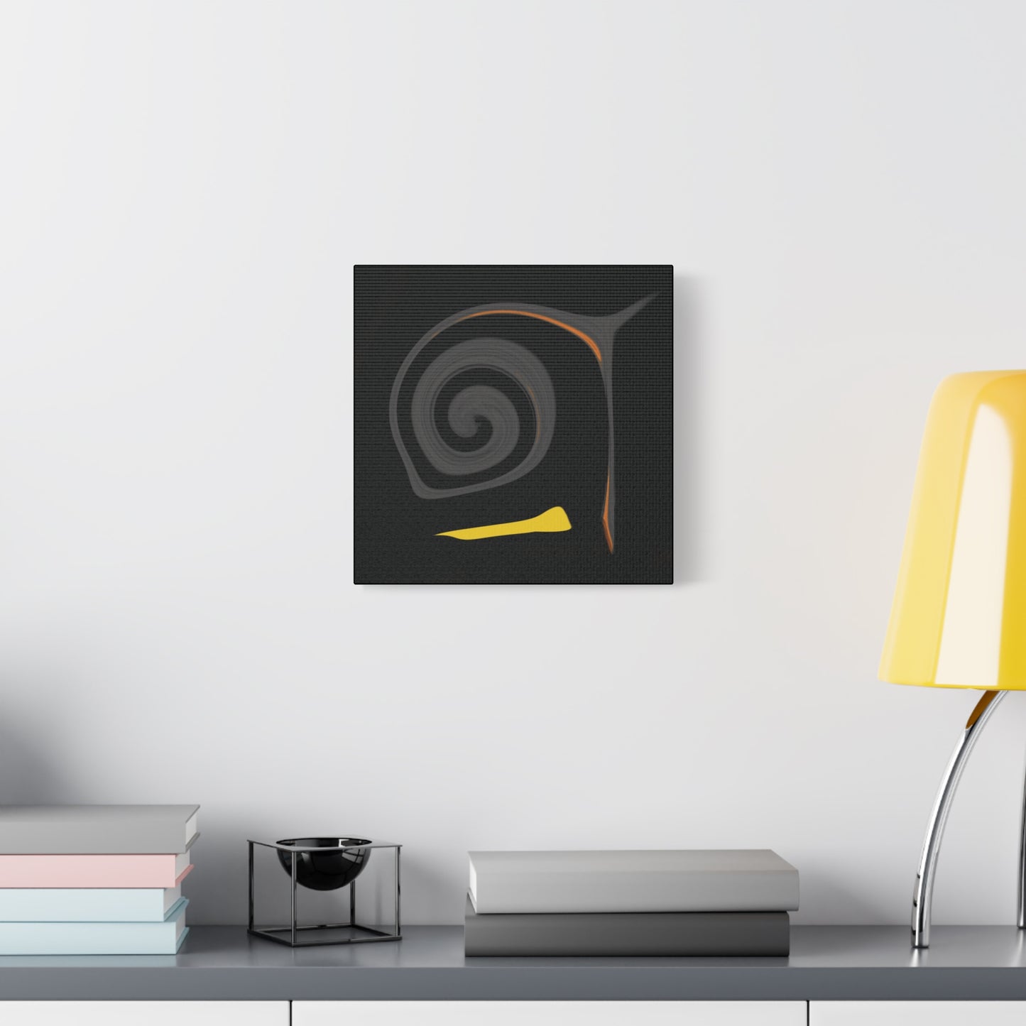 Abstract art piece on a wall above a desk with books and a lamp.