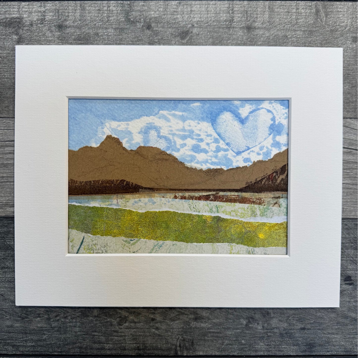 Image of a matted landscape artwork on a grey wooden floor.