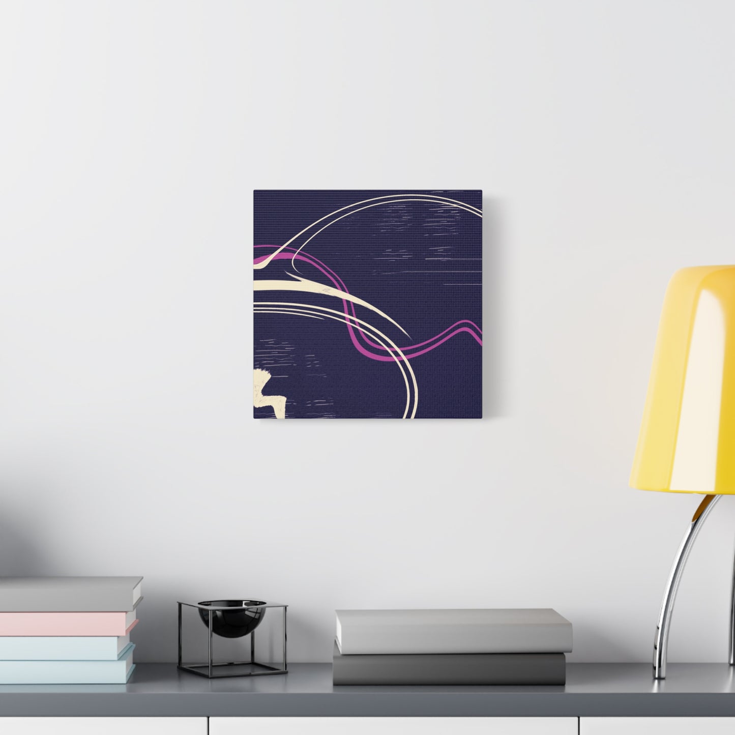 Abstract canvas wall art on a wall above a desk with books and a lamp.