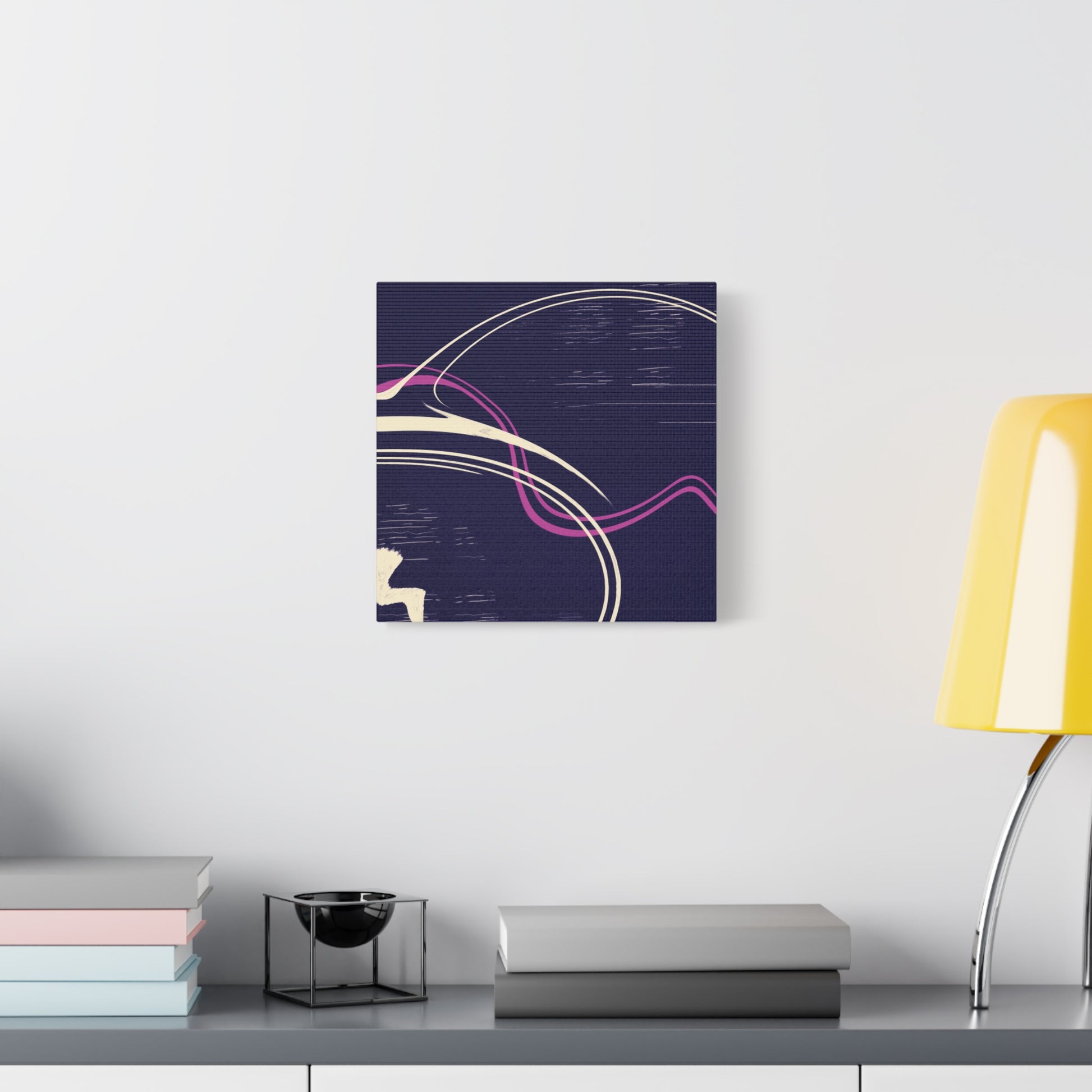 Abstract canvas wall art on a wall above a desk with books and a lamp.