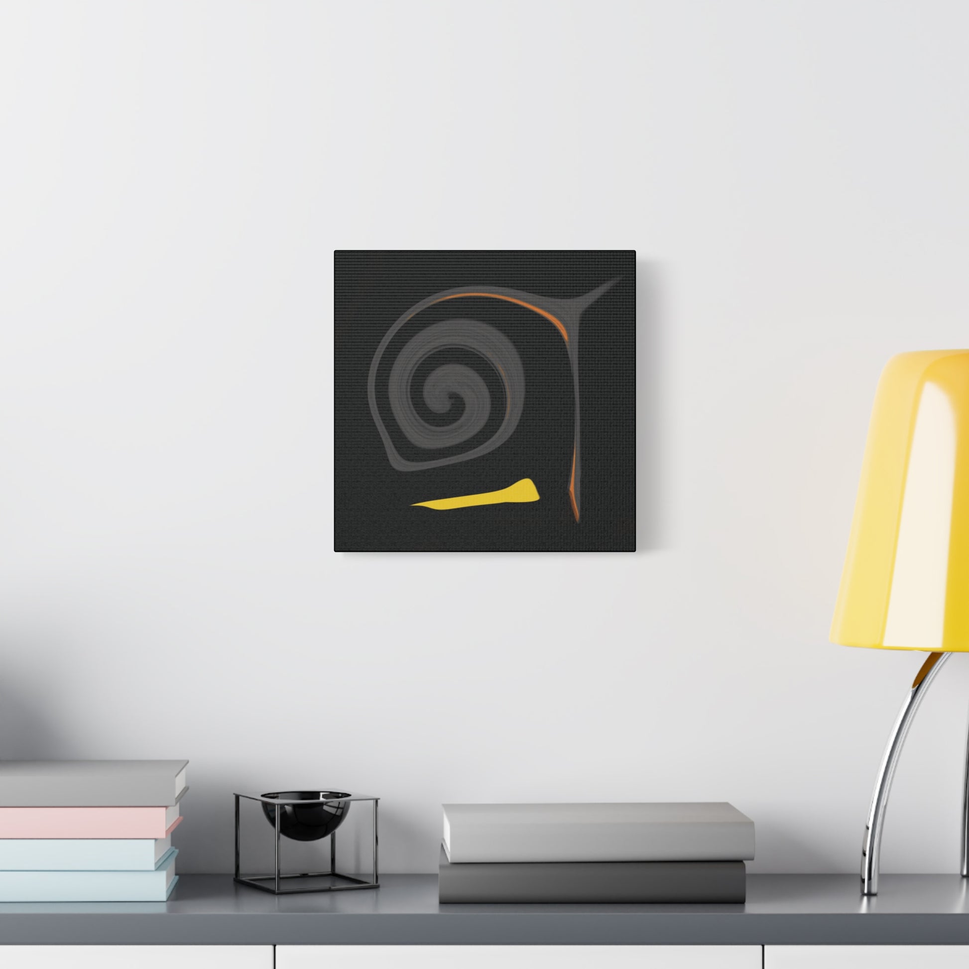 Abstract art piece on a wall above a desk with books and a lamp.