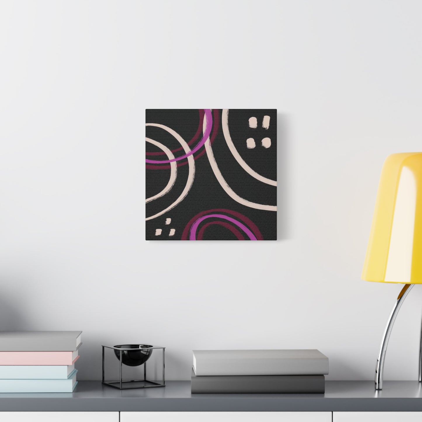 Abstract canvas wall art on a wall above a desk with books and a lamp.