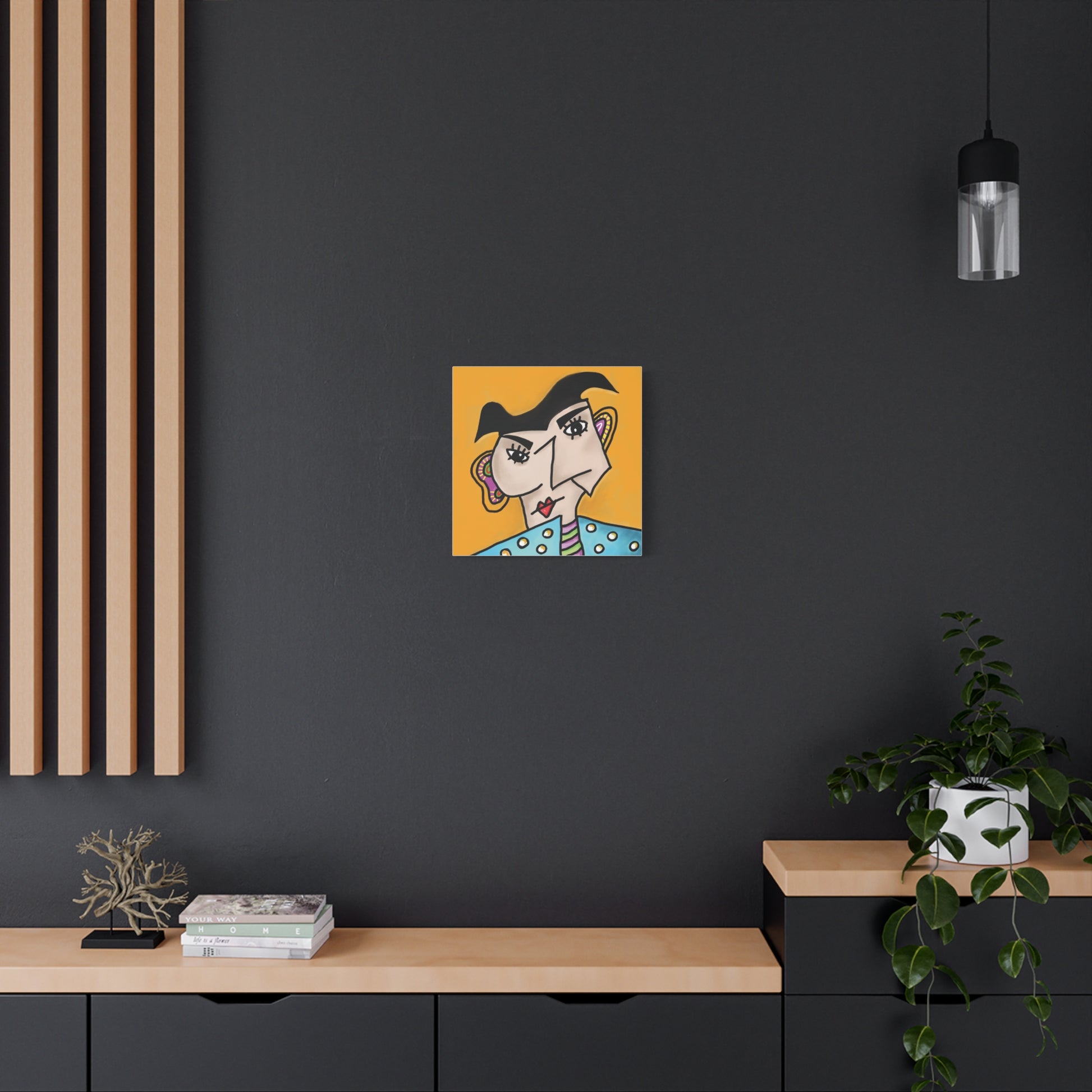 Abstract artwork of a face on an orange background hanging on a dark wall with a wooden shelf and plant below.