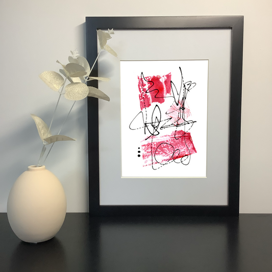 Image featuring an original abstract artwork by artist Julia Hargreaves.  The artwork features three pieces of handcrafted collage in shades of red and free flowing line work.  It is shown in a black frame on a shelf next to a ceramic vase.
