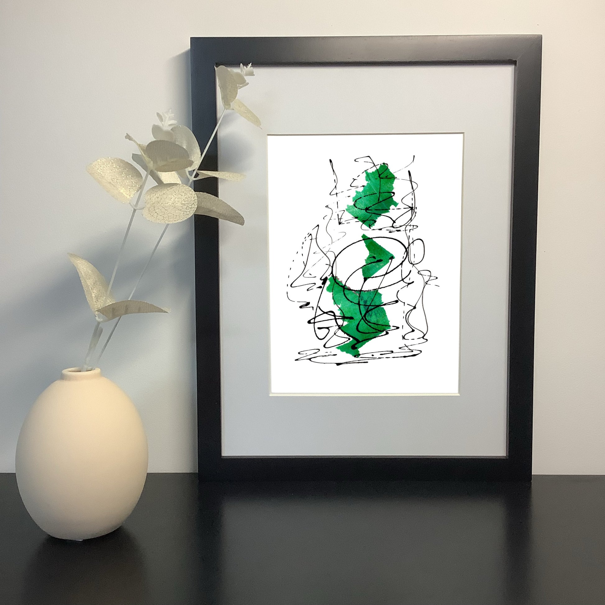 Image featuring a framed artwork on a shelf with a  ceramic vase and foliage.  The artwork by Julia Hargreaves features an expressive abstract design with green and black tones.